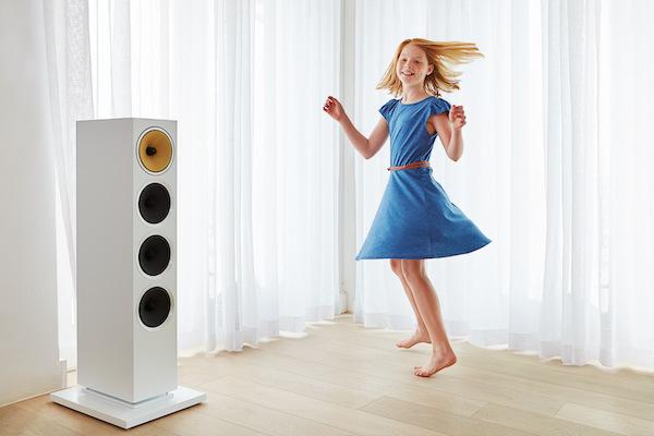 gird in blue dress dancing in corner of room with a white speaker